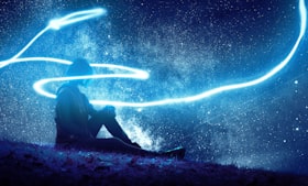 Mulher sentada sob um gramado em noite estrelada com feixe de luz envolvendo-a 