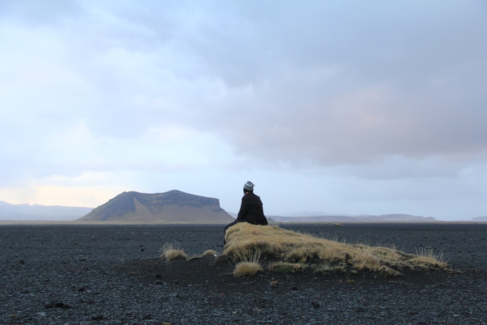 homme assis sur un rocher brun au milieu du désert