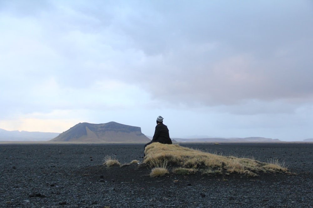 man sitting on brown rock in middle of desert