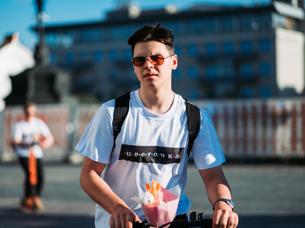 man wearing white and multicolored crew-neck t-shirt and sunglasses standing near bike