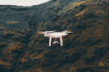 A fixed-wing UAV soaring high above rugged terrain during a survey mission.