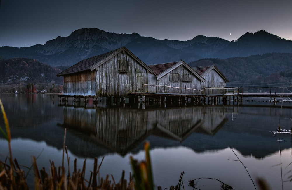 Casa de madeira cinza perto do lago vendo a montanha sob céus cinzentos