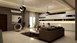 A modern living room features a sleek brown sofa surrounded by decorative pillows. A coffee table with a plant and decorative objects sits nearby, while bookshelves line the back wall with accent lighting. The room is well-lit with contemporary pendant lights, and a large window with sheer curtains allows natural light to filter in. An art print, an air conditioning unit, and a unique round chair complete the stylish decor.