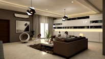 A modern living room features a sleek brown sofa surrounded by decorative pillows. A coffee table with a plant and decorative objects sits nearby, while bookshelves line the back wall with accent lighting. The room is well-lit with contemporary pendant lights, and a large window with sheer curtains allows natural light to filter in. An art print, an air conditioning unit, and a unique round chair complete the stylish decor.