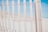 A wooden fence with thin vertical slats held together by horizontal wires is positioned on a sandy beach under a clear blue sky. The sun casts soft shadows, creating a bright and serene atmosphere.