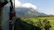 A smiling woman enjoying the view from a geee rail passenger car window with lush green mountains in the background.