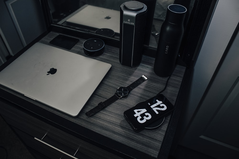 Apple MacBook Air, analog watch and black smartphone on table