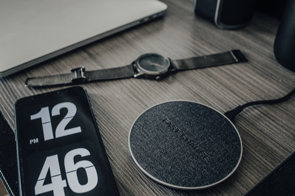 grayscale photo of analog watch, smartphone, and wireless charging pad