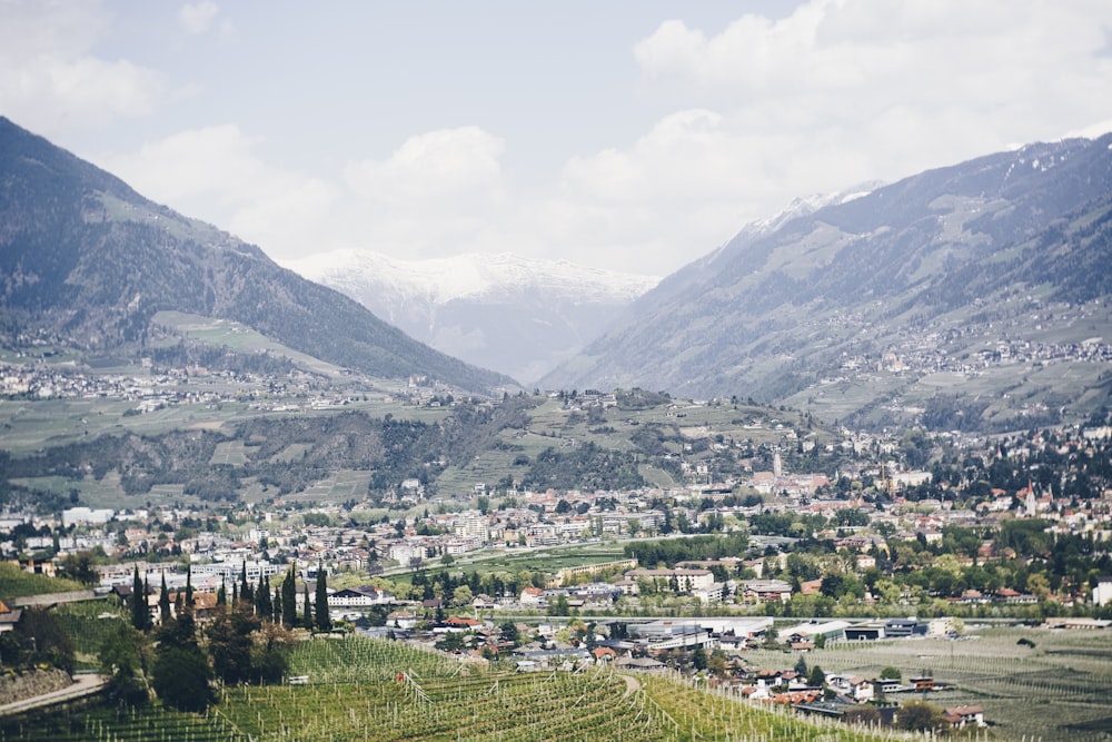 ville avec des immeubles de grande hauteur montrant un champ vert et une montagne sous un ciel bleu et blanc