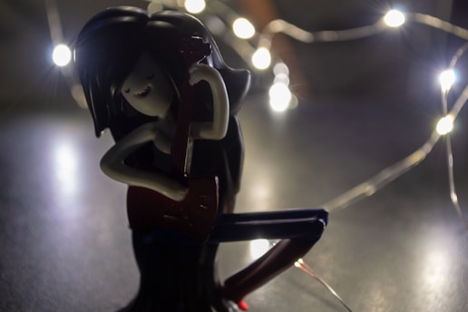 A figure with long black hair is playing a red guitar, surrounded by glowing string lights. The ambient lighting creates a moody and atmospheric scene.