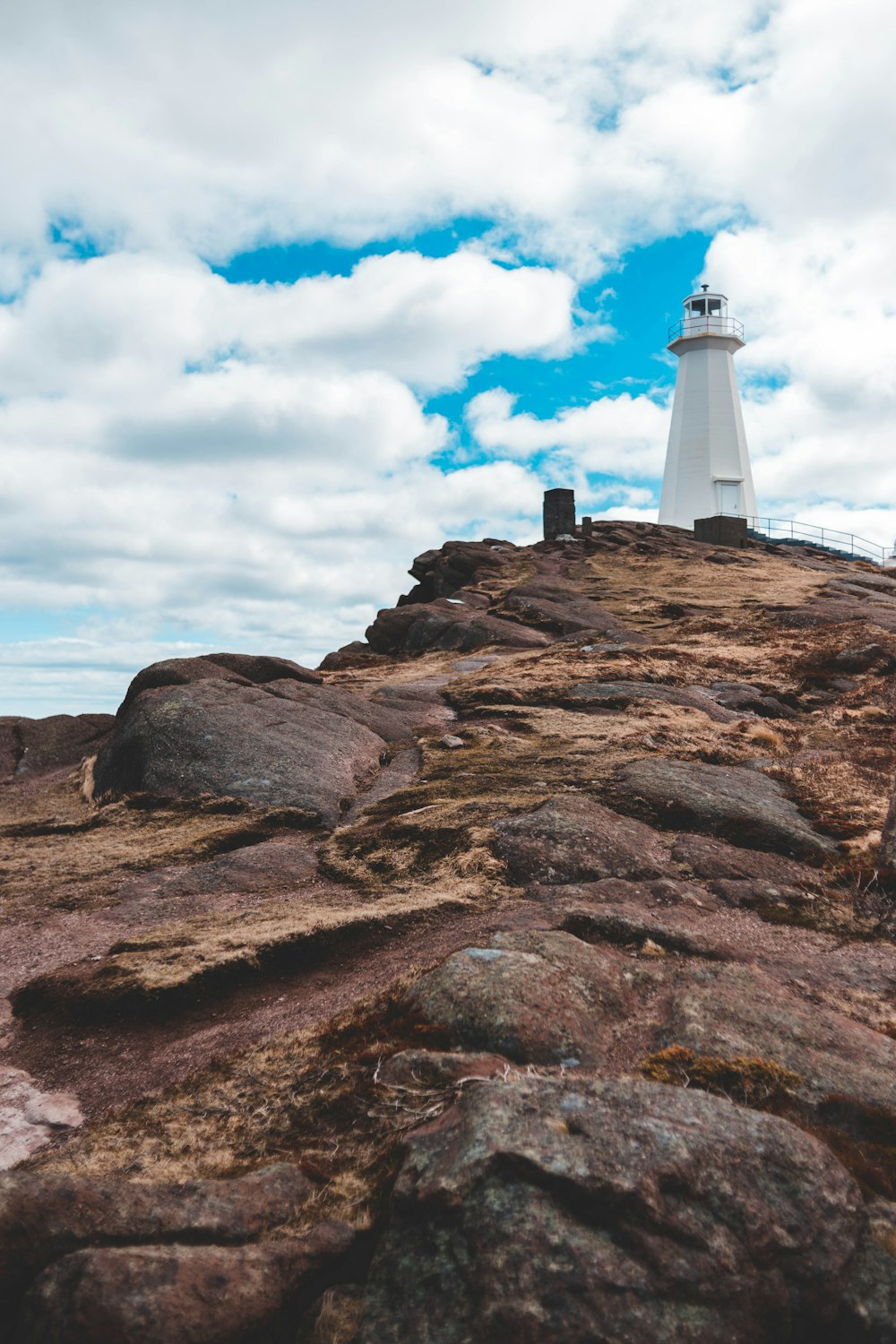 white lighthouse on mountain cliff under cloudy sky during daytime