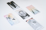 Several tarot cards are spread out on a white surface. Each card features unique illustrations, such as a lion, a crescent moon with forest trees, a pair of flying birds, a deer beneath a rainbow, and two intertwined sticks.