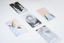 Several tarot cards are spread out on a white surface. Each card features unique illustrations, such as a lion, a crescent moon with forest trees, a pair of flying birds, a deer beneath a rainbow, and two intertwined sticks.