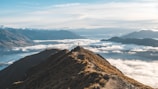 A panoramic view of the rugged Himalayan mountains with a lone hiker standing on a ridge.