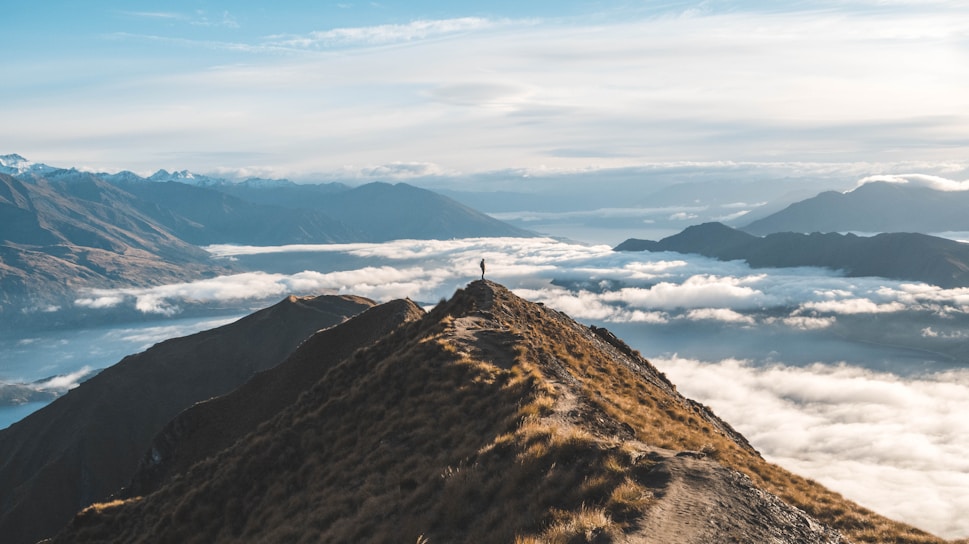 A hiker standing atop a lush green peak with panoramic views of Mauritius' rugged coastline at sunrise.
