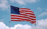 A waving American flag prominently displayed against a backdrop of a bright blue sky with scattered white clouds.