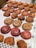 A variety of baked pastries are displayed on a tray. There are swirled, circular pastries with glossy surfaces in red and brown hues. Rectangular pastries with a topping that appears to be rhubarb are visible, as well as several croissant-like pastries with flaky, golden brown crusts.