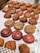 A variety of baked pastries are displayed on a tray. There are swirled, circular pastries with glossy surfaces in red and brown hues. Rectangular pastries with a topping that appears to be rhubarb are visible, as well as several croissant-like pastries with flaky, golden brown crusts.