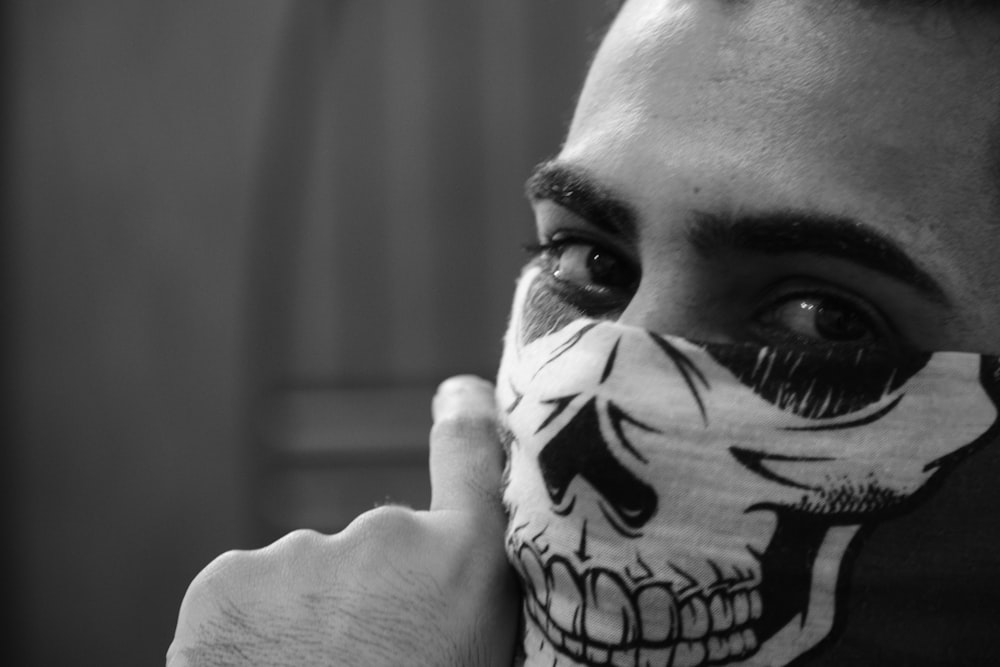 grayscale photo of person covered his mouth with skull printed scarf