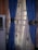 A pair of blue curtains with intricate golden tiebacks is partially covering a window. Behind them, sheer curtains featuring a subtle pattern allow light to filter through. An air conditioning unit is visible on the left side of the image.