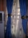 A pair of blue curtains with intricate golden tiebacks is partially covering a window. Behind them, sheer curtains featuring a subtle pattern allow light to filter through. An air conditioning unit is visible on the left side of the image.