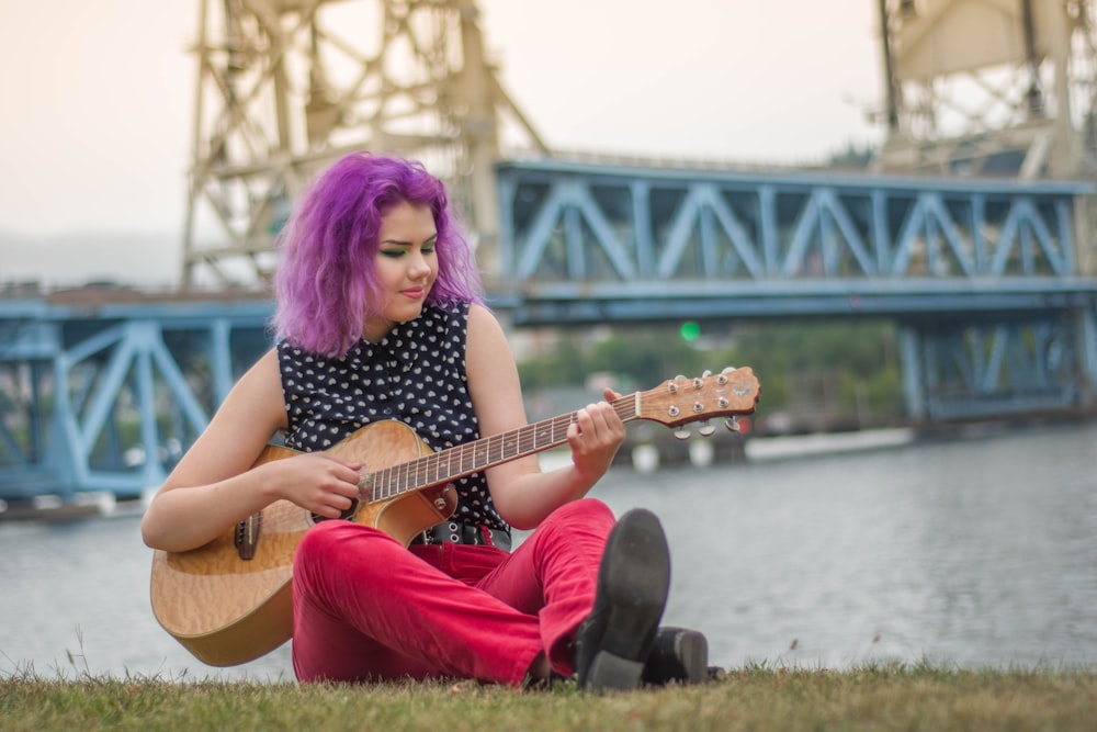 Femme portant une chemise noire assise sur l’herbe tout en jouant de la guitare