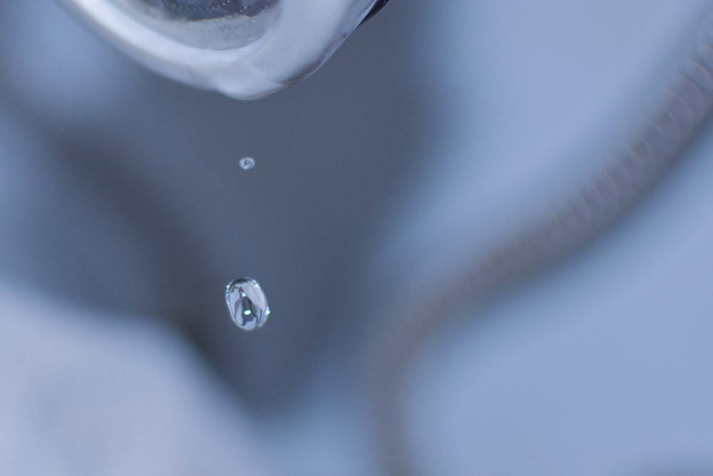 a close up of a sink faucet with a drop of water
