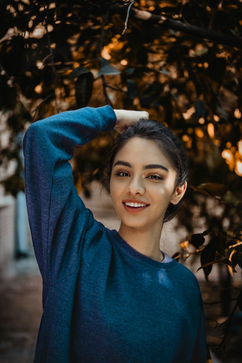 fille portant un pull bleu à col rond debout près de l’arbre pendant la journée