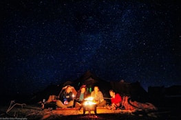 Happy travelers sharing a moment around a campfire under a starry sky.