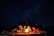 Group of friends laughing around a campfire under starry sky.