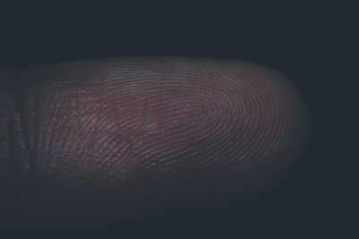 A close-up view of a human fingertip showing detailed fingerprint ridges and grooves, with minimal lighting highlighting the texture of the skin.