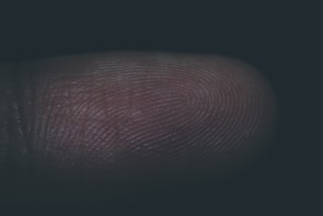 A close-up view of a human fingertip showing detailed fingerprint ridges and grooves, with minimal lighting highlighting the texture of the skin.