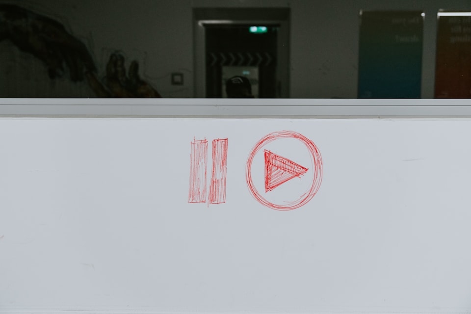 A pause and play symbol drawn in red on a dry erase board