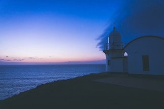 A serene lighthouse glowing softly against a twilight sky over calm waters.