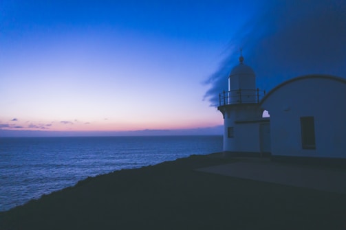 A serene lighthouse glowing softly against a twilight sky over calm waters.