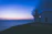 A serene navy blue lighthouse glowing warmly against a twilight sky.