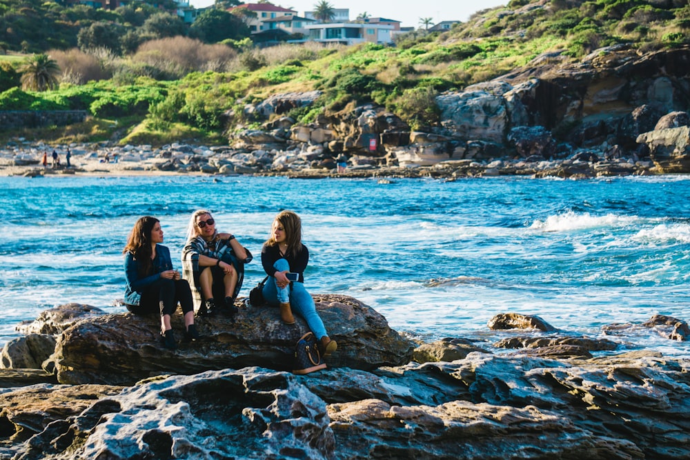 three women sitting on rocks near river