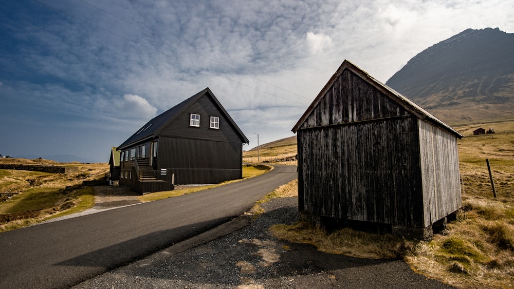 empty concrete road in between brown wooden shed and barn at daytime