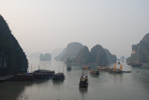 A serene sunrise over the limestone karsts of Halong Bay with a traditional wooden cruise boat gliding through calm waters.