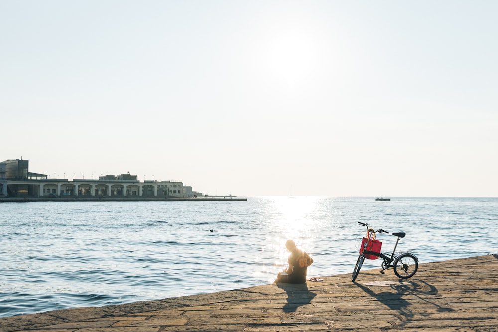 personne assise sur le rivage à côté d’une bicyclette