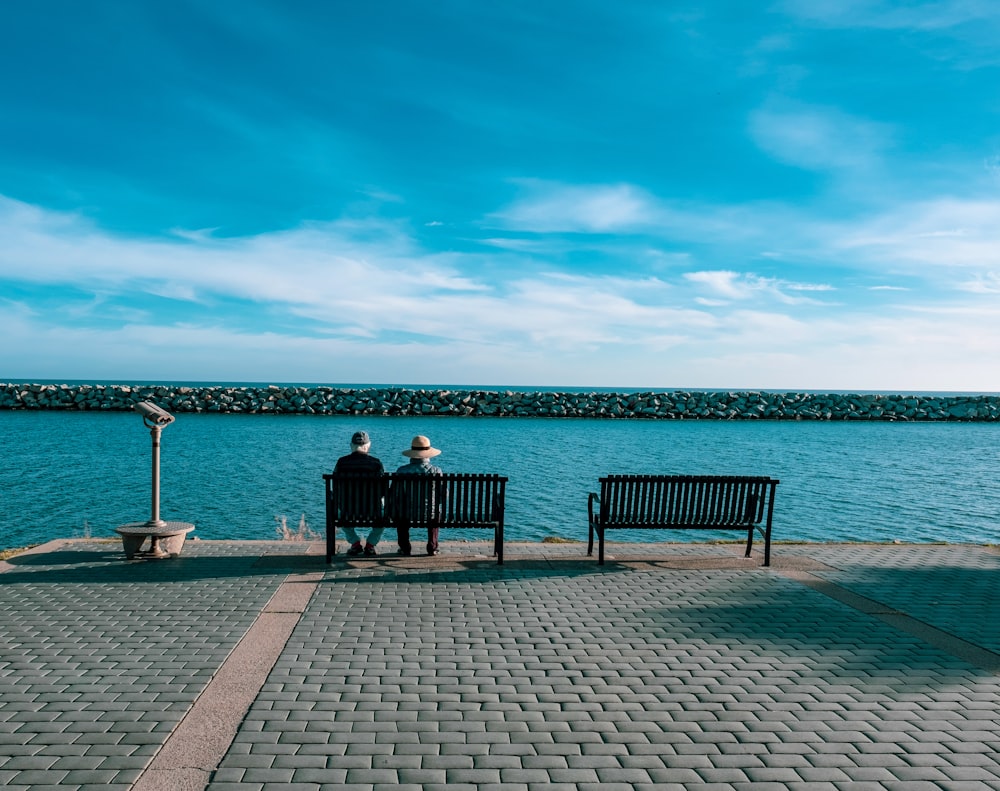 person sitting on black wooden bench in front of body of water during daytime