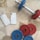 Two smartphones are placed on a tiled floor alongside a dumbbell with interchangeable weights. The dumbbell has blue and red weight plates, and the smartphones have sleek metallic finishes. The setting suggests a combination of technology and fitness.