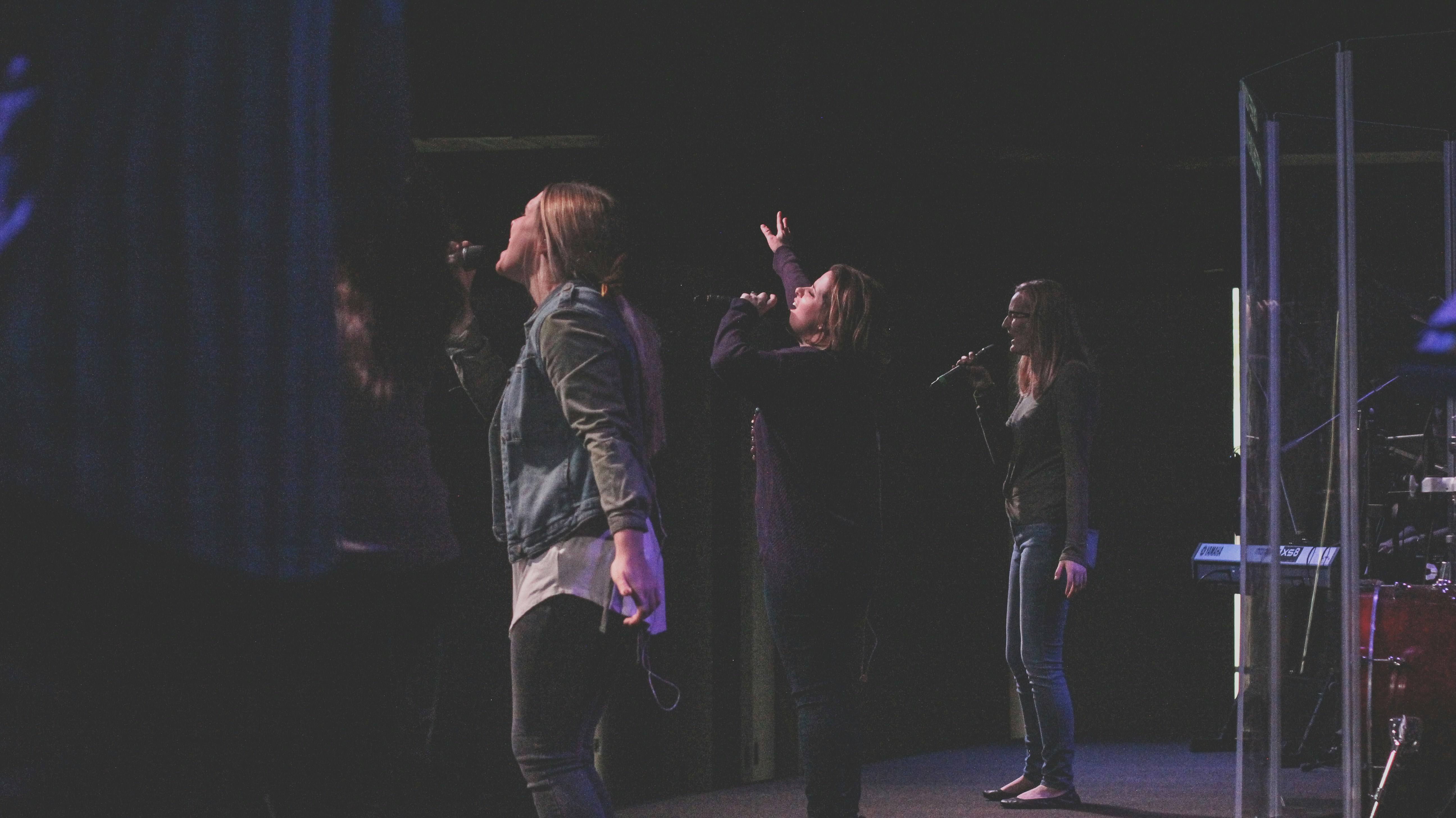 three women singing near stage during nighttime