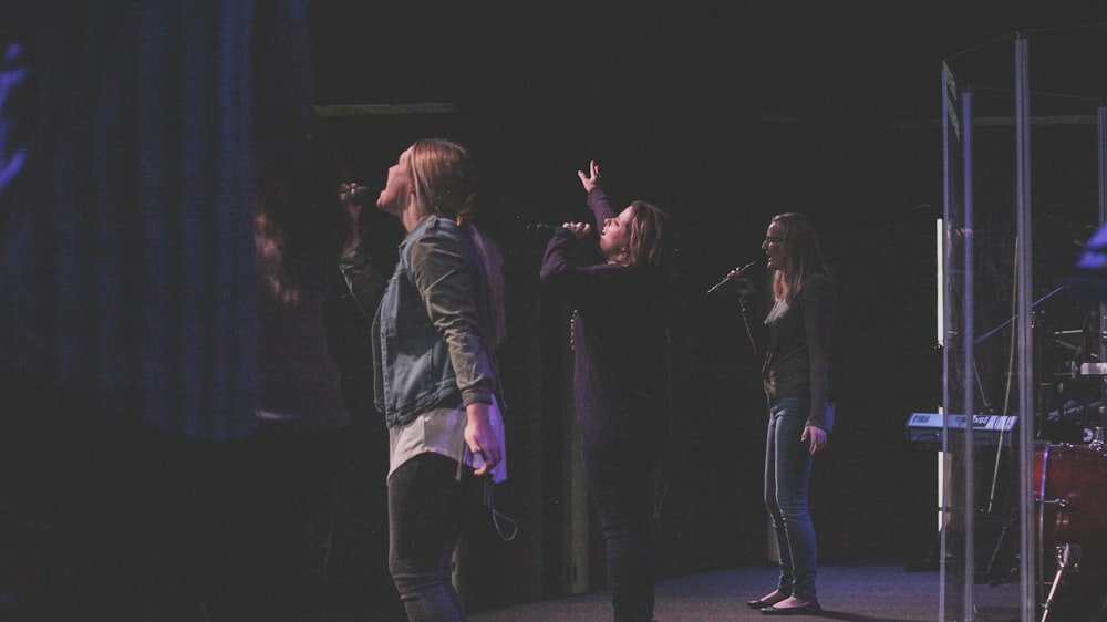 three women singing near stage during nighttime