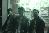 A group of friends laughing in bold streetwear, standing under a glowing urban neon sign.