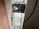 A metal bracket is attached to the edge of a textured surface. The bracket is secured by screws to a white plastic or composite material. A black cable is visible running in the background.