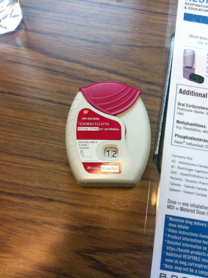 A respiratory therapist demonstrating proper inhaler technique to a patient in a bright, welcoming clinic room.