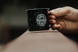 A hand holding a matte black mug outdoors with soft natural light highlighting its smooth finish.