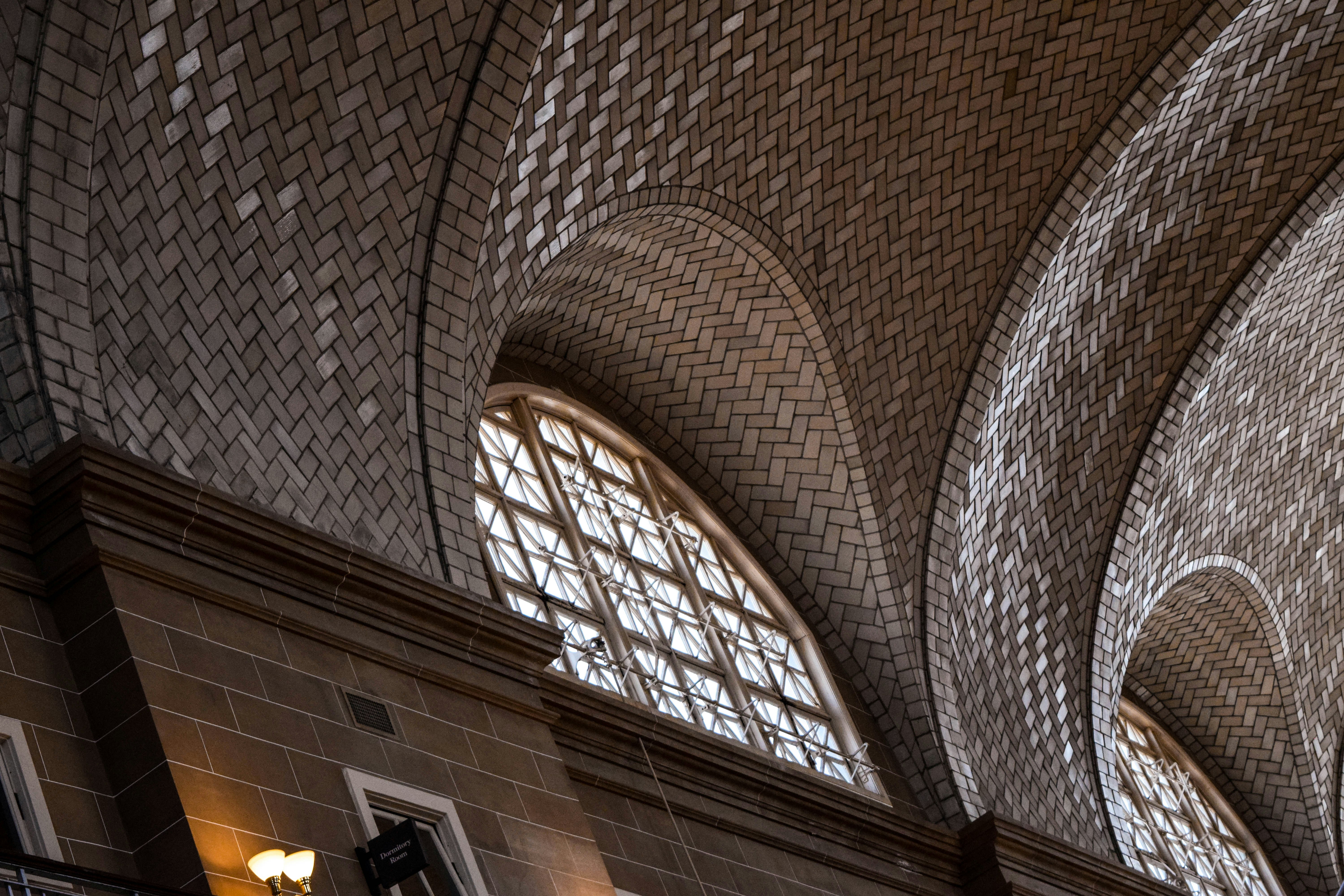 A detailed, close-up view of an architectural structure with a series of curved, tiled archways and large, grid-patterned windows. The interior features elegant design elements and warm lighting emanating from wall sconces.
