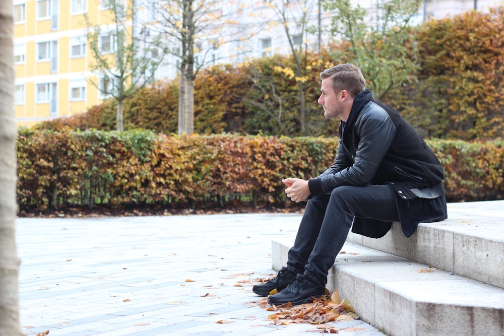 man wearing black jacket sitting on stair steps